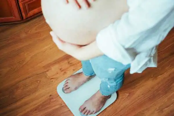 Image of woman weighing herself and experiencing weight gain through pregnancy Atherstone